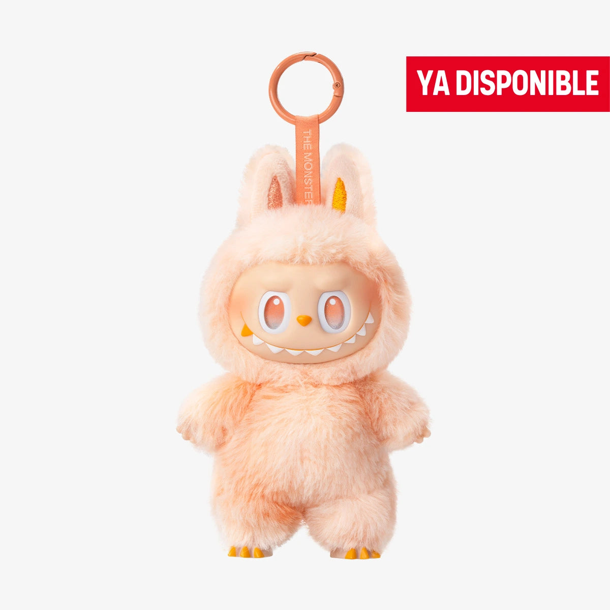 Llavero coleccionable de Labubu de la serie "Big Into Energy", con traje de peluche color durazno, ojos anaranjados vibrantes y sonrisa afilada característica. Tiene orejas de conejo visibles y detalles en amarillo en las garras y el interior de las orejas. Cuelga de una anilla naranja con cinta que dice "THE MONSTERS". En la esquina superior derecha aparece una etiqueta roja con el texto "YA DISPONIBLE"