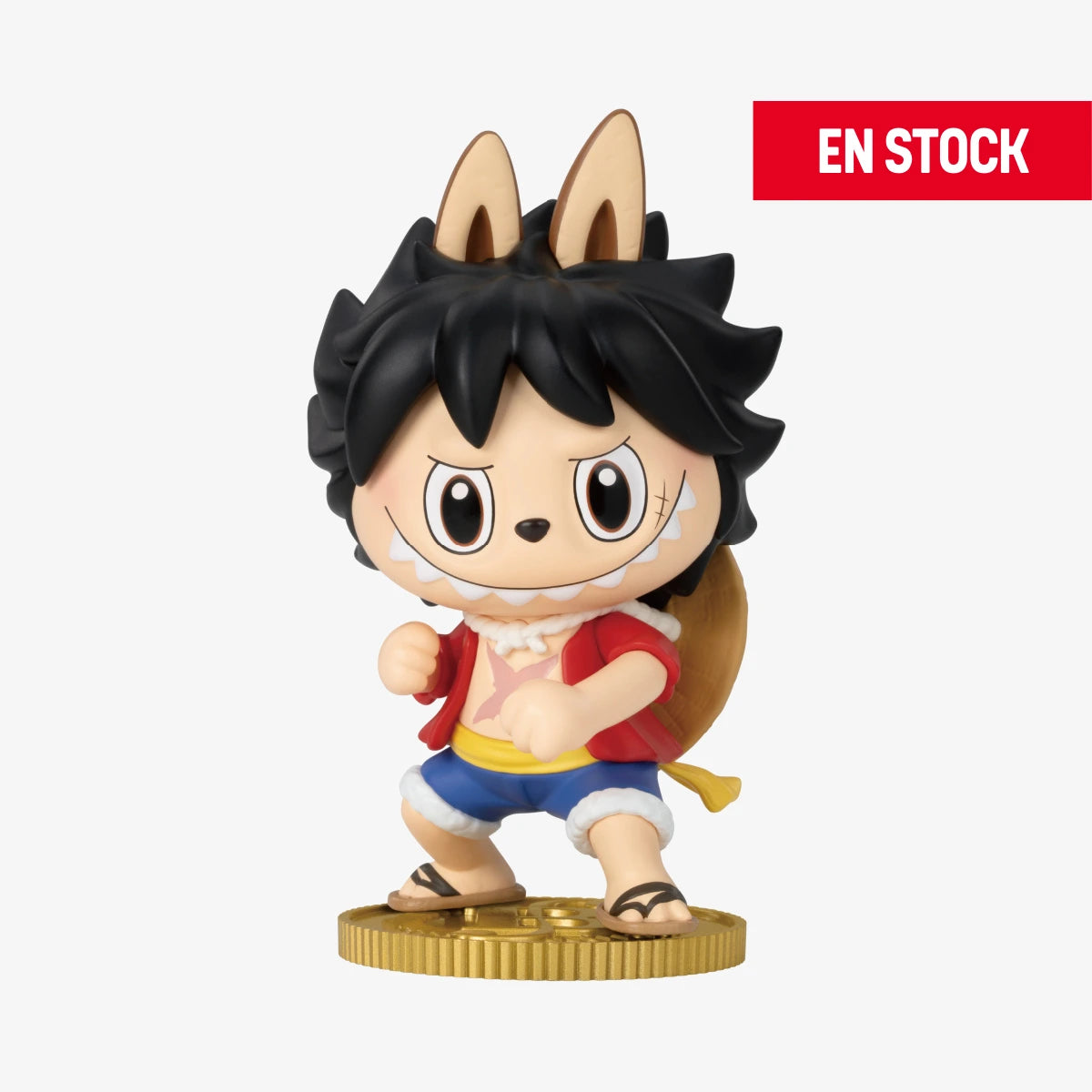 Figura coleccionable de Labubu con disfraz de Luffy de One Piece, luciendo cabello negro despeinado, chaqueta roja, pantalones cortos azules y mochila. Está en pose de combate sobre una base dorada con expresión decidida. En la esquina superior derecha aparece una etiqueta roja con el texto