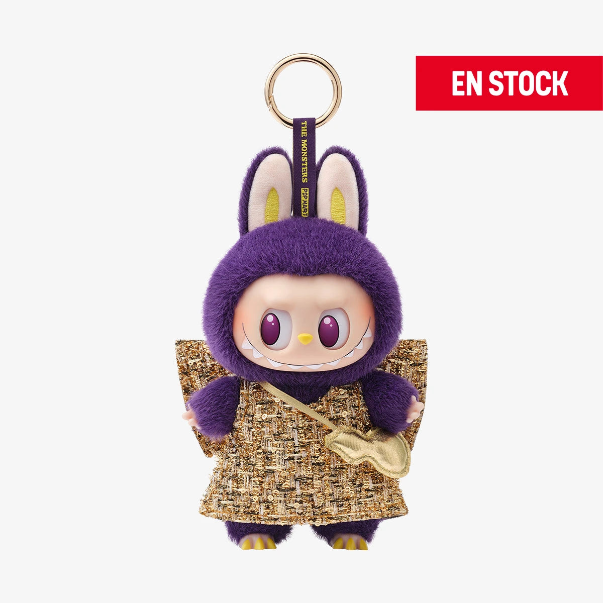 Llavero coleccionable de Labubu de la serie "Wings of Fortune", con traje de peluche morado, vestido dorado de tela tejida y una pequeña bolsa dorada cruzada. Tiene orejas de conejo visibles, ojos morados brillantes y una sonrisa traviesa. Cuelga de una anilla dorada con cinta que dice “THE MONSTERS”. En la esquina superior derecha aparece una etiqueta roja con el texto "EN STOCK"