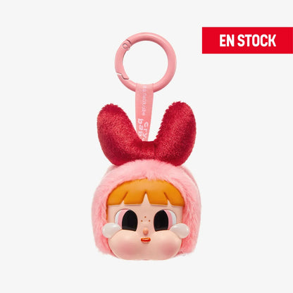 Llavero coleccionable de la colaboración CRYBABY × Powerpuff Girls, con cabeza de peluche rosa, lazo rojo de felpa y rostro de personaje con mejillas redondeadas, ojos grandes y cabello naranja. Incluye anilla rosada para colgar y cinta con la marca. En la esquina superior derecha aparece una etiqueta roja con el texto EN STOCK