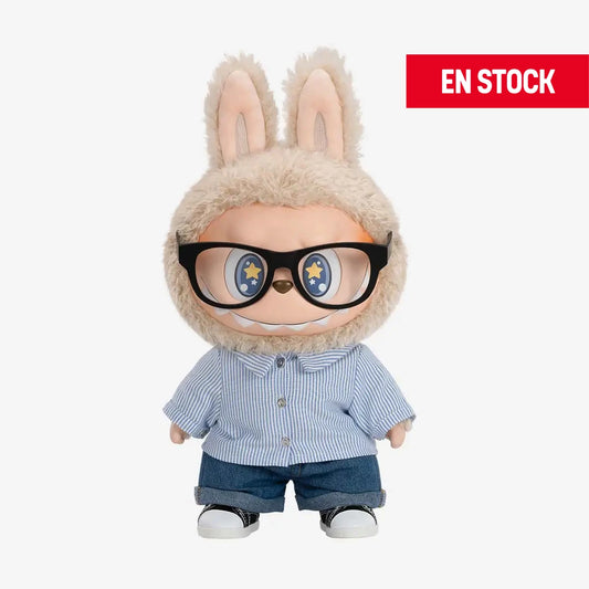 Figura coleccionable de Labubu de la serie "Flip With Me", con traje peludo beige, lentes grandes negros y expresión sonriente con ojos decorados con estrellas. Viste una camisa de rayas azul claro, pantalones de mezclilla y tenis blancos con negro. En la esquina superior derecha aparece una etiqueta roja con el texto "EN STOCK"