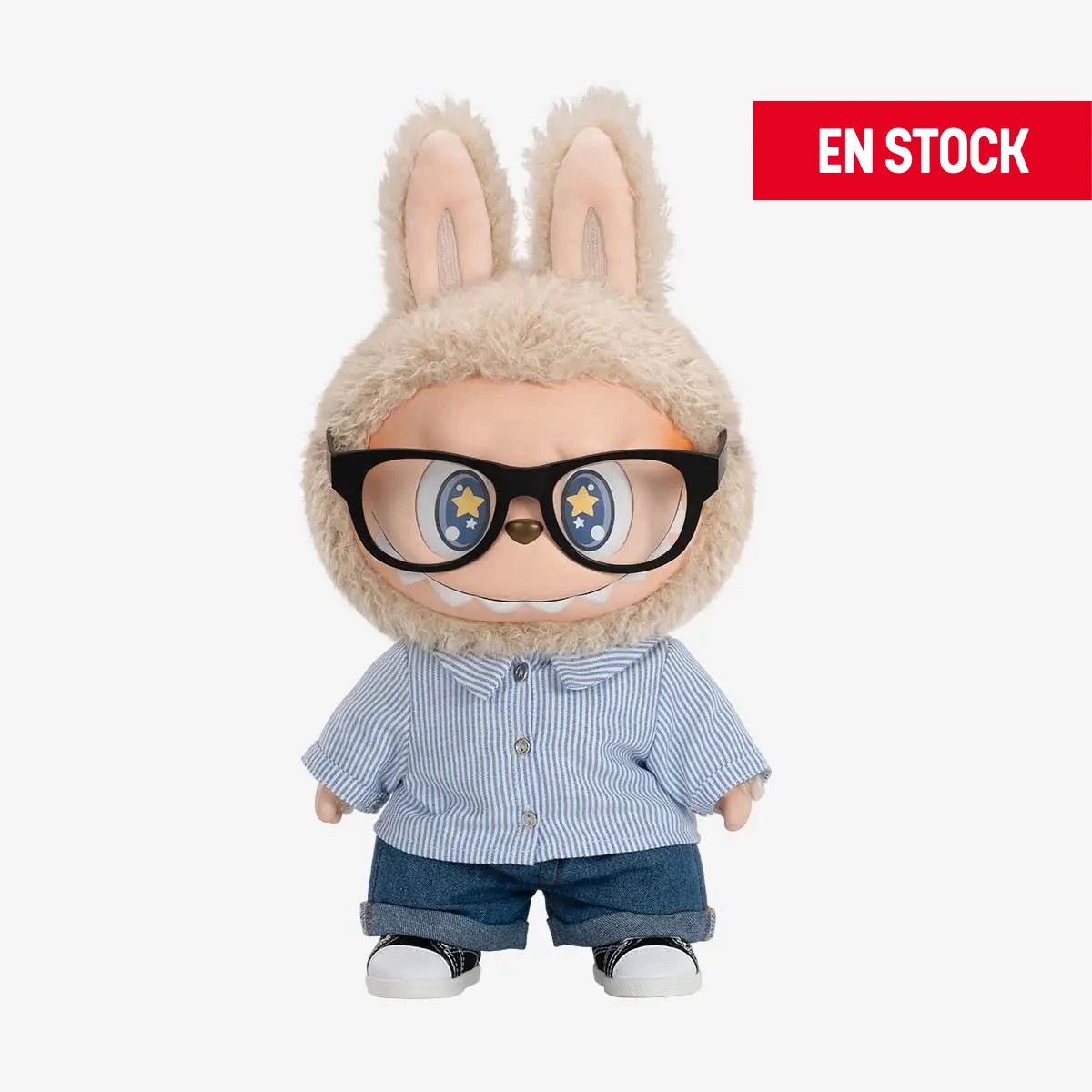 Figura coleccionable de Labubu de la serie "Flip With Me", con traje peludo beige, lentes grandes negros y expresión sonriente con ojos decorados con estrellas. Viste una camisa de rayas azul claro, pantalones de mezclilla y tenis blancos con negro. En la esquina superior derecha aparece una etiqueta roja con el texto "EN STOCK"