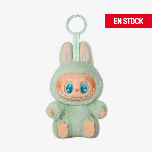 Llavero coleccionable de Labubu de la serie "Have a Seat", con traje de peluche verde menta y orejas de conejo. Labubu está en posición sentada con expresión sonriente y ojos grandes color turquesa. Cuelga de una anilla verde con cinta que dice “THE MONSTERS”. En la esquina superior derecha aparece una etiqueta roja con el texto "EN STOCK"