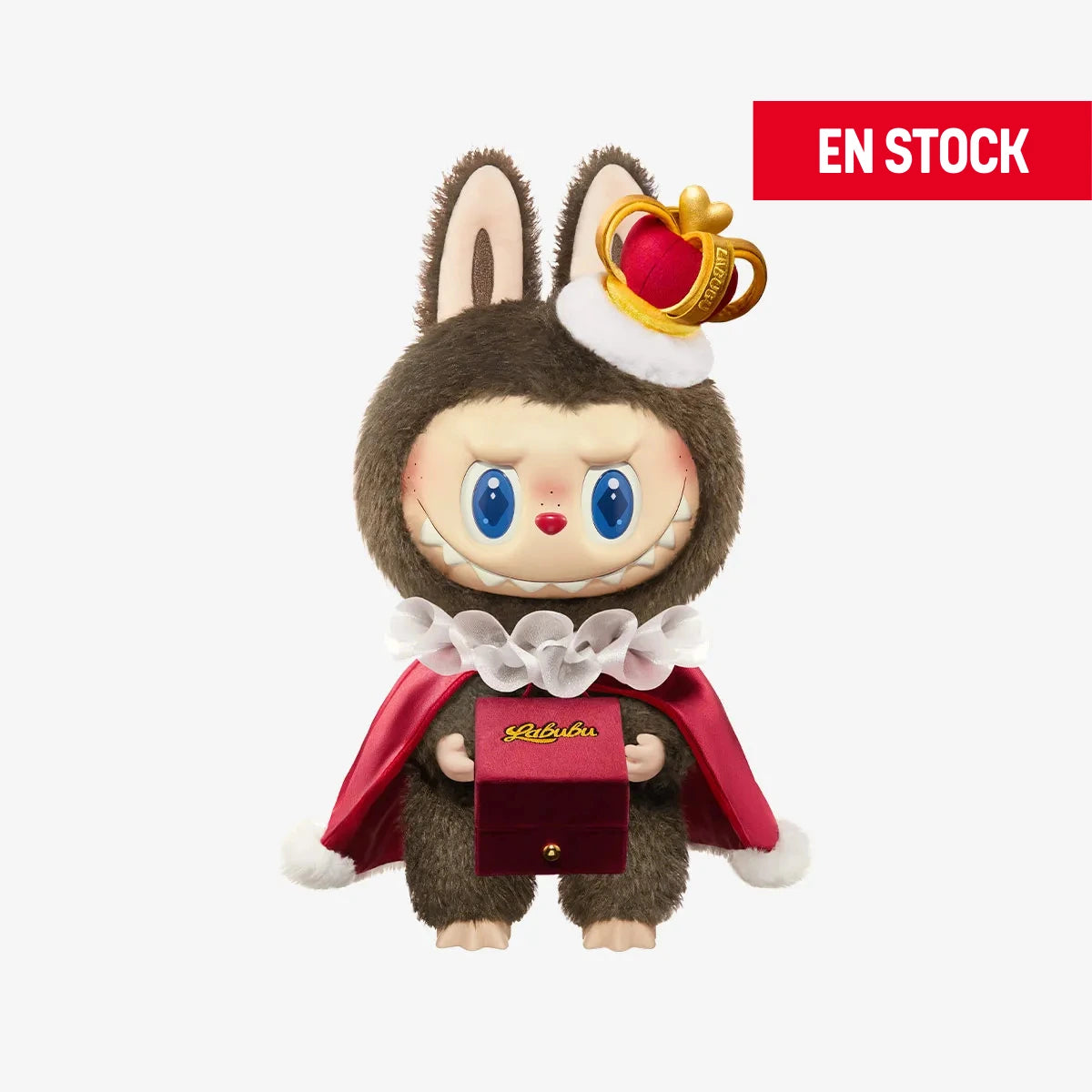 Figura coleccionable de Labubu con temática de San Valentín, vestido como rey con un traje marrón de peluche, capa roja con cuello blanco de volantes y una corona pequeña inclinada sobre la cabeza. Sostiene una caja de terciopelo rojo con la palabra "Labubu" escrita en dorado. En la esquina superior derecha aparece una etiqueta roja con el texto "EN STOCK"