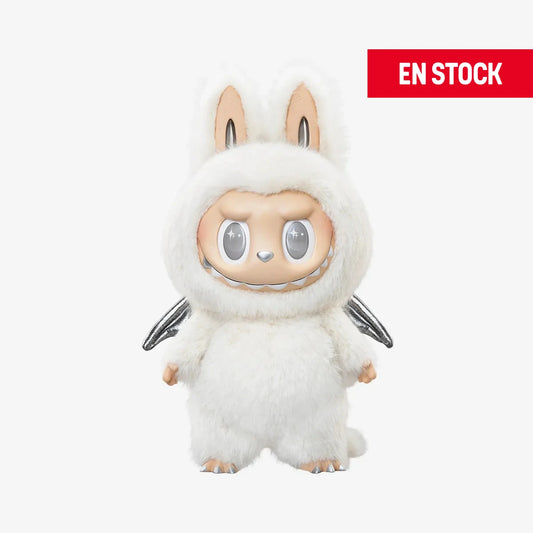 Figura coleccionable de Zimomo con temática de ángel, vestido con un traje esponjoso blanco de orejas largas y alas plateadas. El personaje tiene expresión seria y ojos plateados brillantes, con detalles suaves y acabados de alta calidad. En la esquina superior derecha aparece una etiqueta roja con el texto "EN STOCK"